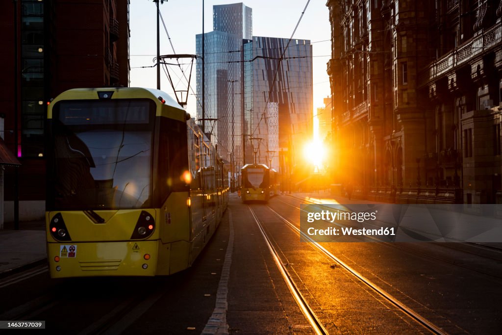 UK, England, Manchester, Cable cars moving along downtown street at sunset