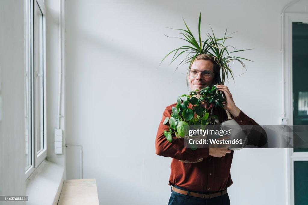Businessman talking on smart phone and standing with plants in front of wall