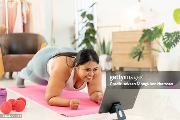 young overweight woman watching an exercising video at home while exercising - postura de plancha fotografías e imágenes de stock