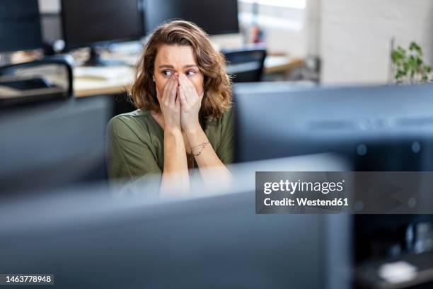 worried businesswoman covering face sitting in office - angst stockfoto's en -beelden