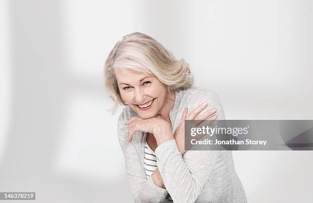 mature woman with arms resting on hand laughing - touching skin stock pictures, royalty-free photos & images