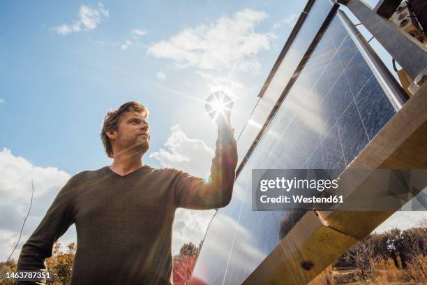 mature man standing by solar panels on sunny day - forced perspective stock pictures, royalty-free photos & images