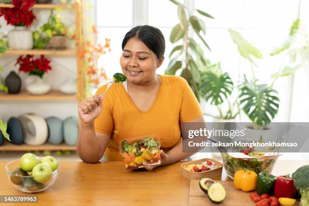 overweight woman at home eating delicious healthy vegetable salad in her kitchen. - big fat women stock pictures, royalty-free photos & images