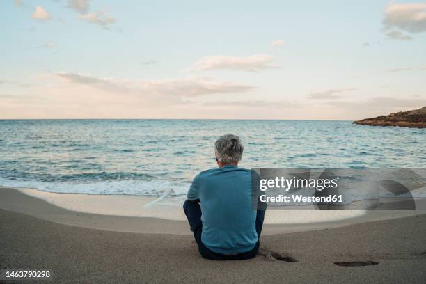 senior man sitting on sand in front of sea at beach - twilights fotografías e imágenes de stock