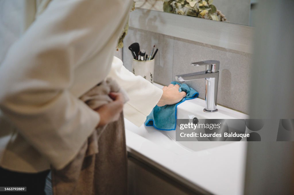 Close up view of the hands of a mature white woman cleaning the faucet with a disinfectant wiper