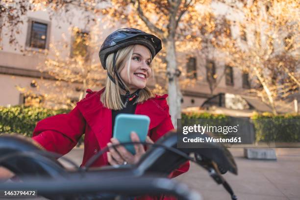 happy mature woman holding smart phone riding bicycle - kombinerad mobilitet bildbanksfoton och bilder