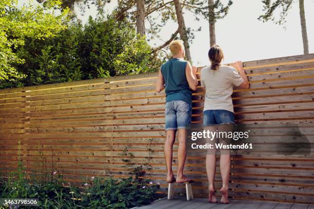 young couple looking over wooden fence at back yard - über etwas schauen stock-fotos und bilder