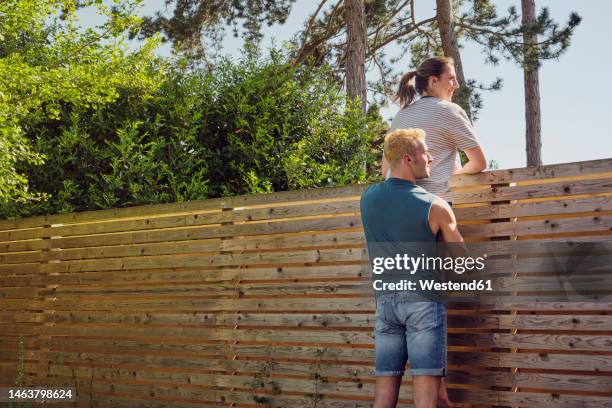 happy man carrying woman looking over wooden fence at back yard - looking over fence stock pictures, royalty-free photos & images