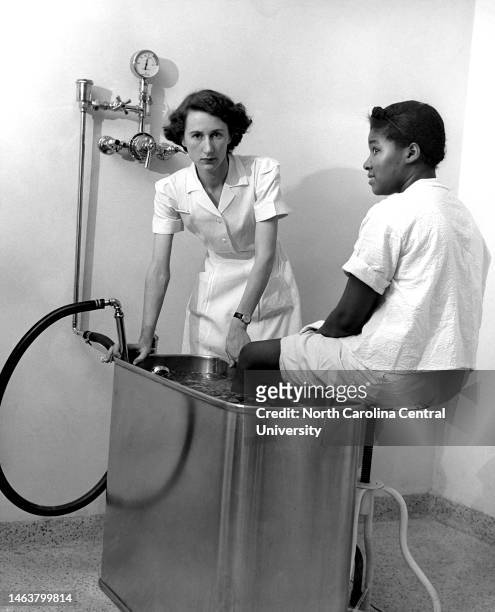 Nurse standing by woman at water container. Jean Gordon, P.T., was the first trained physical therapist at Lincoln Hospital. Pictured here c. 1953,...