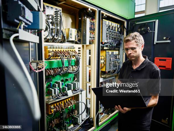 technician using laptop at machine in modern factory - mechatronics stock-fotos und bilder