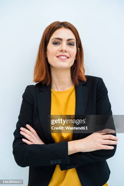 smiling businesswoman standing with arms crossed against white background - waist up photos et images de collection