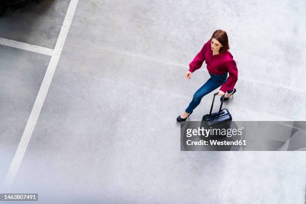businesswoman with wheeled luggage walking at parking lot - trolley stock-fotos und bilder