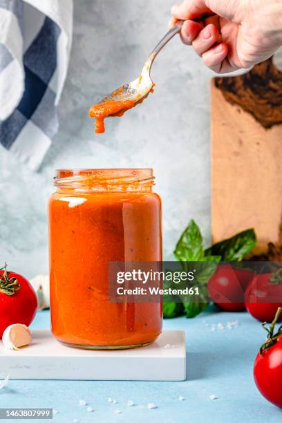 hand of woman holding spoon with tomato sauce over jar on table - tomato paste stock pictures, royalty-free photos & images