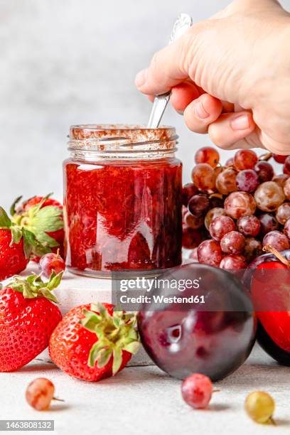 hand of woman holding spoon with homemade strawberry jam on table - strawberry jam stock pictures, royalty-free photos & images