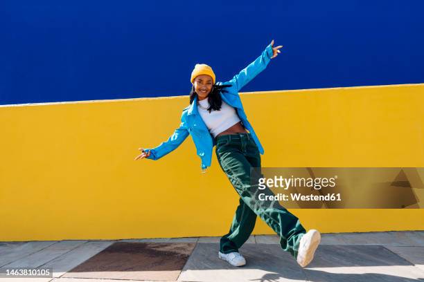 smiling young dancer dancing with arms outstretched on footpath - coolpad stockfoto's en -beelden