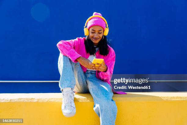 smiling woman with headphones using smart phone on wall - listen to music stockfoto's en -beelden