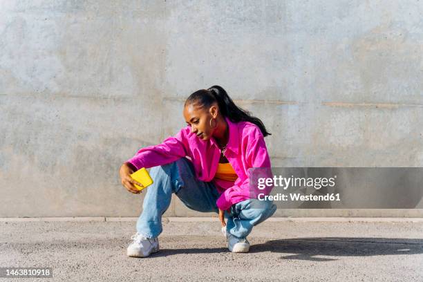 dancer in squatting position taking selfie through smart phone on sunny day - posen stockfoto's en -beelden