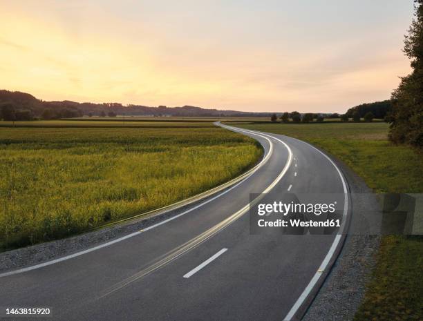 austria, vehicle light trails stretching along country road at dusk - country road stock pictures, royalty-free photos & images