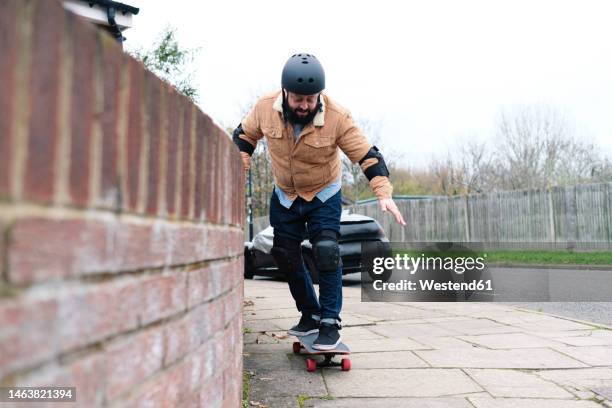 mature man learning skateboarding taking support of wall on footpath - padding 個照片及圖片檔