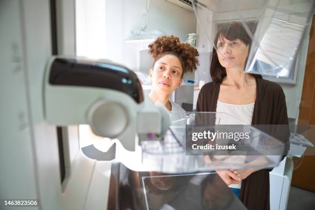 young female medical expert explaining mammography machine to patient in examination room - mammogram stock pictures, royalty-free photos & images