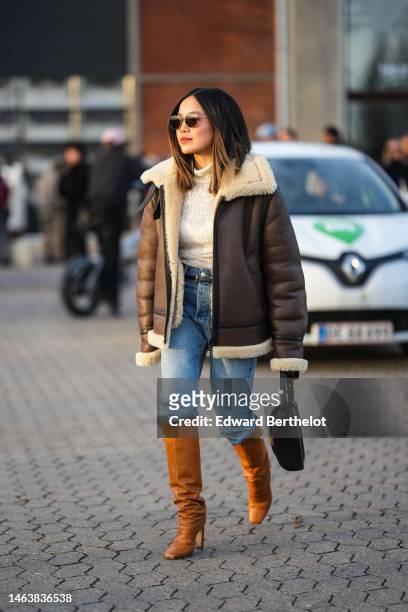 Guest wears black circle sunglasses, a white embossed pattern high neck pullover, a dark brown shiny leather with beige sheep borders oversized...
