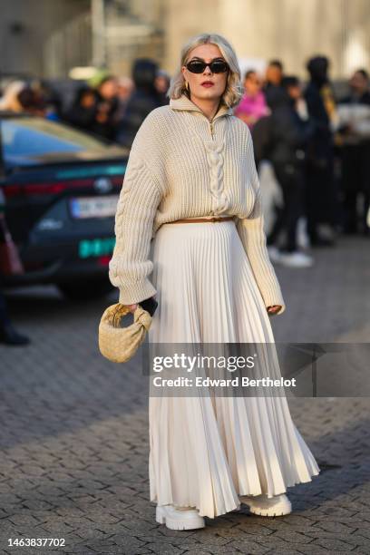 Guest wears black sunglasses, gold earrings, a beige braided wool zipper high neck pullover, a pale yellow braided shiny leather Jodie handbag from...