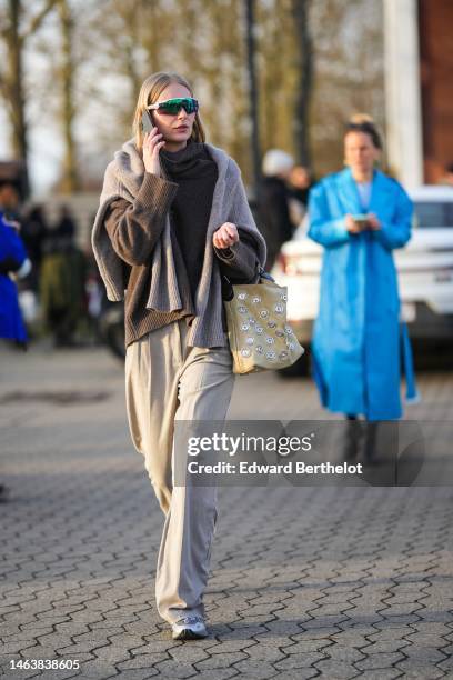 Guest wears futurist sunglasses, a dark brown wool turtleneck pullover, a pale gray wool pullover, beige large suit pants, a beige suede with...
