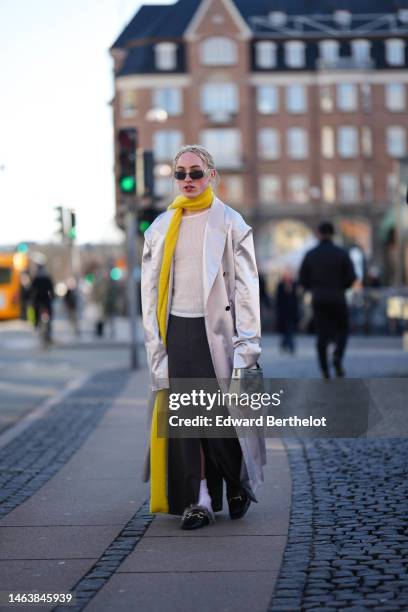 Guest wears black sunglasses from D&G, a silver piercing, a white t-shirt, a white long trench coat, a yellow wool long scarf, a black slit / split...