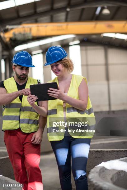 mujer embarazada y hombres jóvenes en la fábrica de construcción que buscan tableta y sonríen - pregnant july 2017 fotografías e imágenes de stock