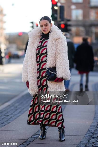 Guest wears gold earrings, a black turtleneck pullover, a white oversized fluffy long coat, a black shiny leather handbag, red shiny leather gloves,...