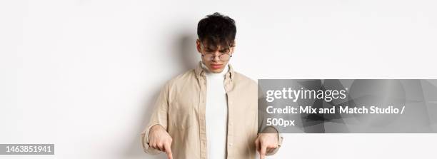 confused frowning guy in glasses looking,pointing fingers down at - face down stock-fotos und bilder