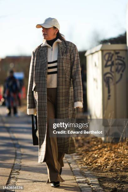 Guest wears a white cap, silver earrings, a black wool turtleneck pullover, a white with black striped print pattern ribbed wool zipper high neck, a...