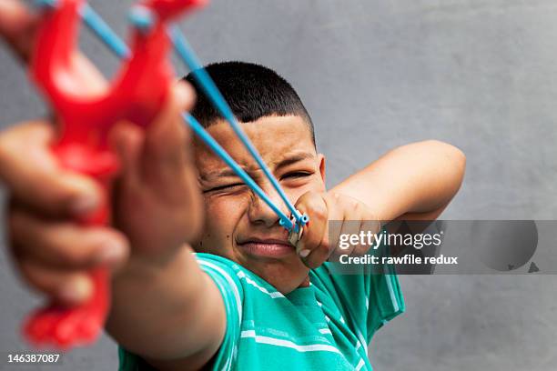 hispanic kid pointing with a slingshot. - zwiesel stock-fotos und bilder