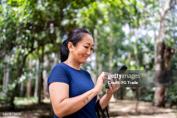 reife frau benutzt mobiltelefon im öffentlichen park - generation x stock-fotos und bilder