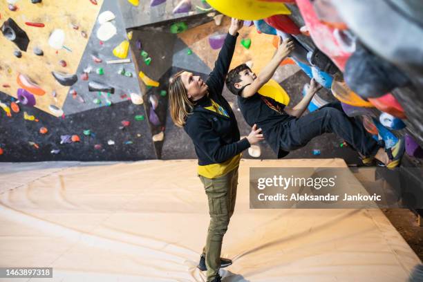 a female climbing coach helping a boy climber solve a boulder problem - bouldering stock pictures, royalty-free photos & images