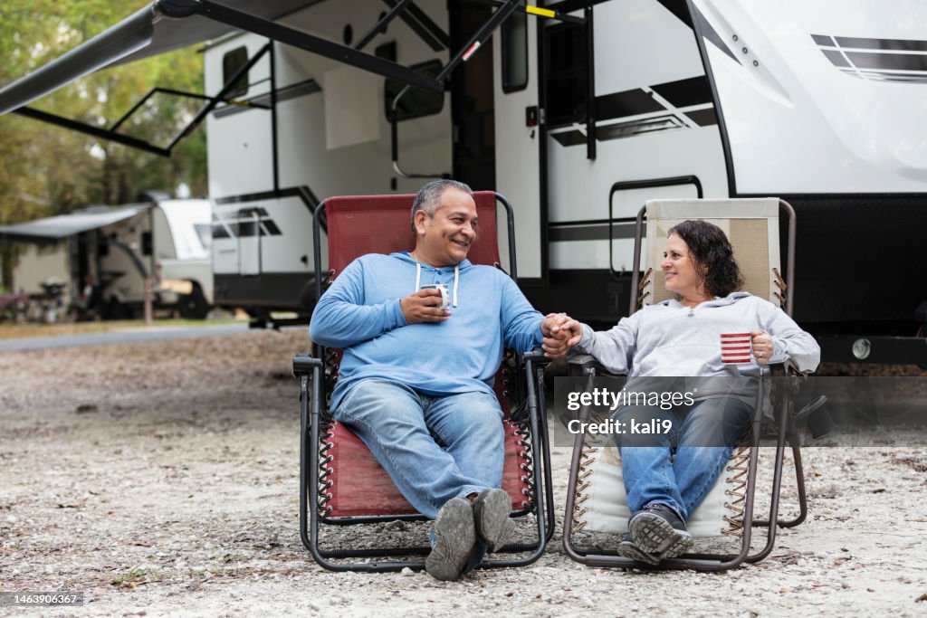 Pareja multirracial sentada en sillas junto a camper en parque de casas rodantes