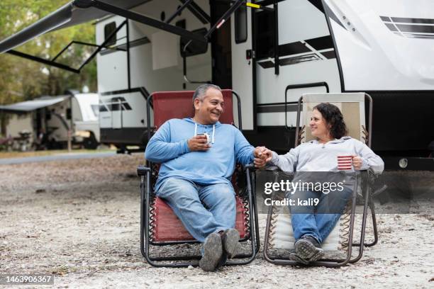 multiracial couple sitting in chairs by camper in rv park - trailer park imagens e fotografias de stock