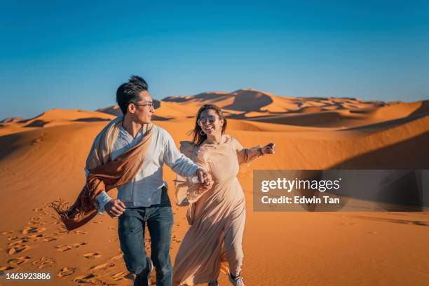 portrait asian chinese couple running in morocco sahara desert - morocco stock pictures, royalty-free photos & images