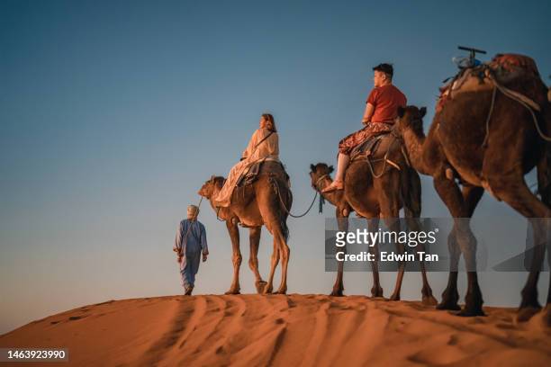 moroccan camel driver leading asian chinese female tourist crossing sahara desert in evening - merzouga stock pictures, royalty-free photos & images