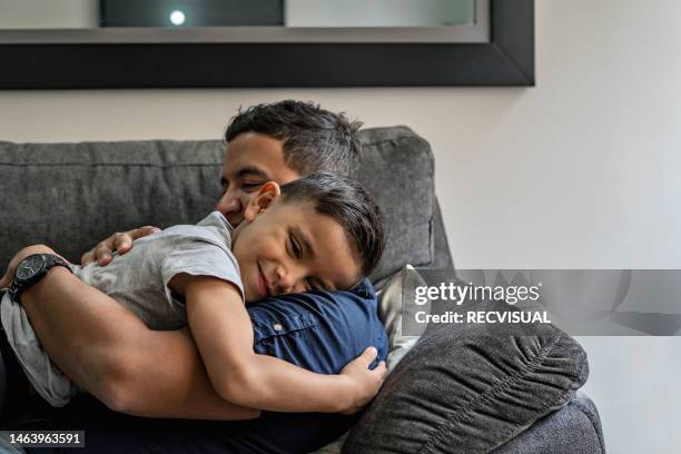 porträt eines vaters und seines sohnes, die sich zu hause umarmen - vatertag stock-fotos und bilder