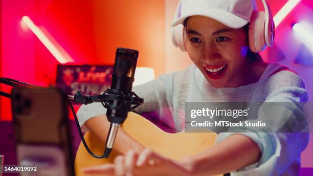 close-up happy asian girl influencer wear headphone with guitar record podcast onair online live streaming talk follower comment and audience on phone at home studio. - content stock pictures, royalty-free photos & images