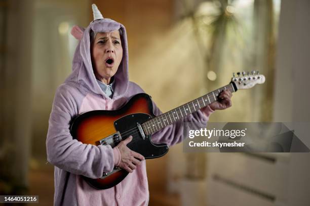 senior woman signing while playing a guitar at home. - crazy old lady stock pictures, royalty-free photos & images