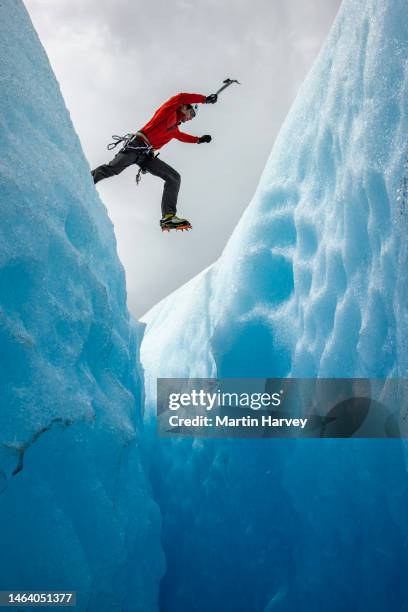 leap of faith.spectacular view of a mountaineer jumping over a large crevasse in a glacier. los glaciares national park, argentina - leap of faith activity stock pictures, royalty-free photos & images