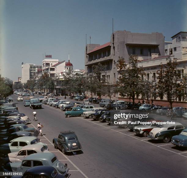 Pedestrians walk past cars parked on Main Street in the centre of the city of Bulawayo in Southern Rhodesia circa 1955. Visible in the background is...