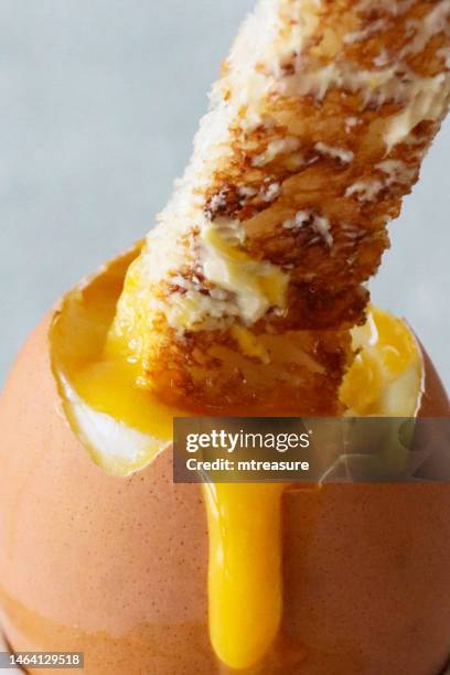 full frame image of white buttered toasted bread slice being dipped into runny yellow yolk of soft boiled egg, marble effect background, focus on foreground - soft boiled egg stock pictures, royalty-free photos & images