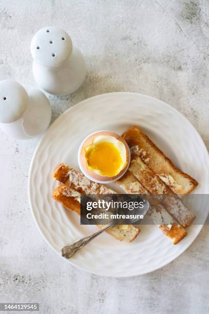 image of soft boiled egg with soldiers, runny yolk, white bread toast slices with butter, white eggcup, metal teaspoon, salt and pepper shaker cruet set, marble effect background, elevated view - pepper pot stock pictures, royalty-free photos & images
