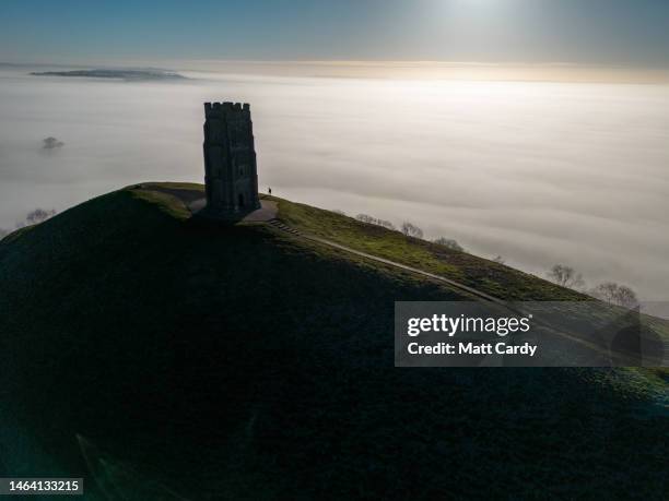 Aerial view of early morning mist, frost and fog lingers in fields surrounding St. Michael's Tower at the top of Glastonbury Tor near the town of...
