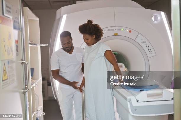 young male doctor helping female patient while stepping down from mri scanner in medical examination room - arm around stock pictures, royalty-free photos & images