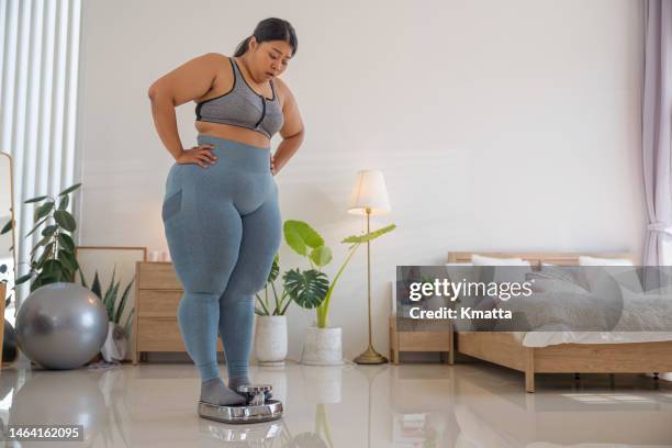 plus size woman weighing herself on a scale. - plus size women stock-fotos und bilder