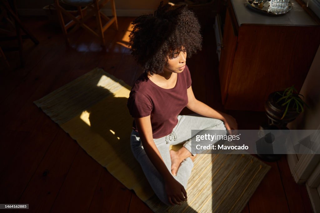 Young African woman meditating by a sunny window at home